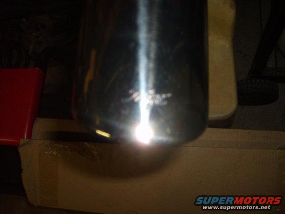 Chrome exhaust pipe with visible scratches and a bright light reflection