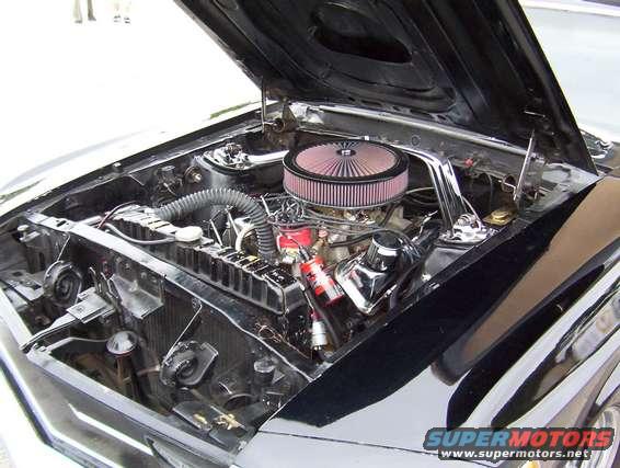 Close-up of a black car's engine bay with a large air filter and chrome accents. Hood is open