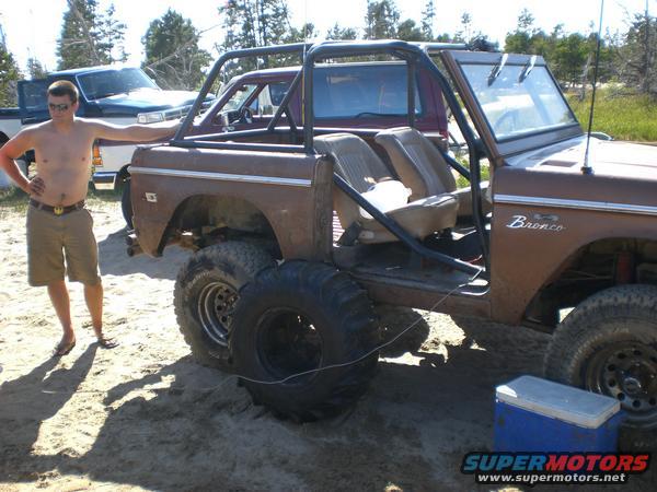 Brown 1976 Ford Bronco with roll cage and large tires, parked on sand