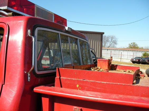 Side view of a red pickup truck with emergency lights on top. Another vehicle is visible in the background