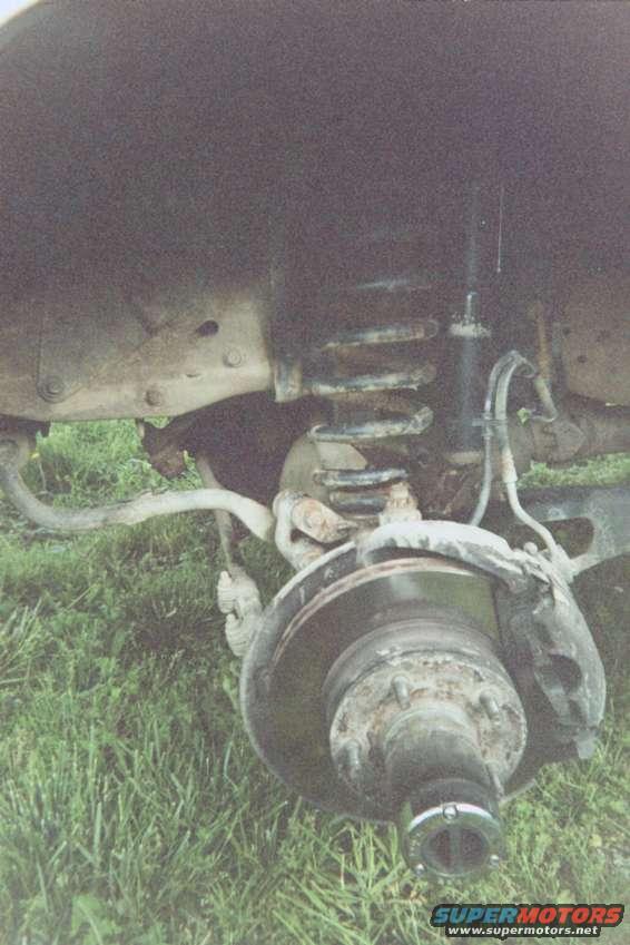 driver_stock__no_tire.jpg Stock driver's side w/tire removed.

The spring hook at the top of the spring is a 13mm (if memory serves) and comes off easily.

The nut in the center of the spring [cup] was an 1 1/8" - I used a combination wrench through the spring coils to break it loose.  Be sure to spray everything down with WD-40 AS SOON AS taking off the tire.  TRUST ME, this will help.  Another hint...jack the axle up to flex the springs to get the combination wrench to the nut easier.

You can also get to the nut with 3 (6")extensions through the access hole in the top of the spring/shock mount.

When all hardware is removed (including shock) remove the jack from under the axle, and either push with one hand (down) on the hub and pull w/the other on the spring OR get your lovely girlfriend to jump on it as you pull out the spring (the later would probably be your best option).