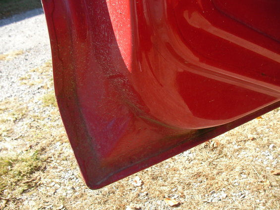 Close-up of the bottom corner of a red vehicle door, showing some dirt and wear
