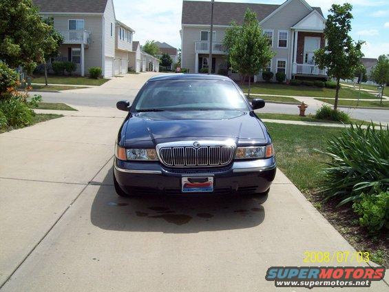 Dark blue sedan parked on a concrete driveway, front view. Chrome grille, rectangular headlights