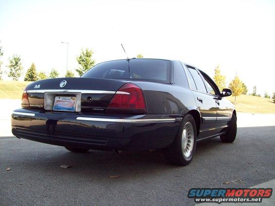 Dark sedan, likely a Mercury Grand Marquis, seen from the rear quarter. License plate is visible