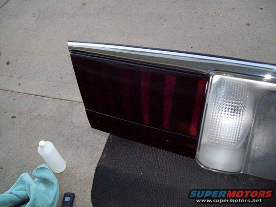 Car tail light assembly with dark red lenses and chrome trim, next to cleaning supplies