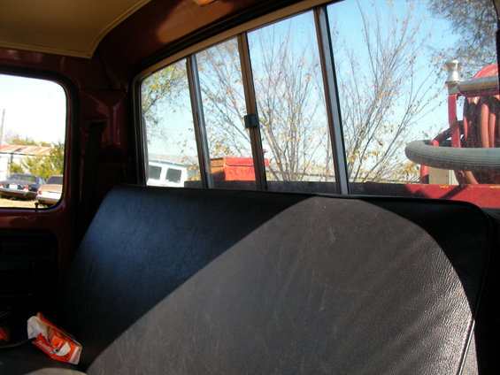 View from inside a truck cab, looking out the back window at trees and two other vehicles parked outside