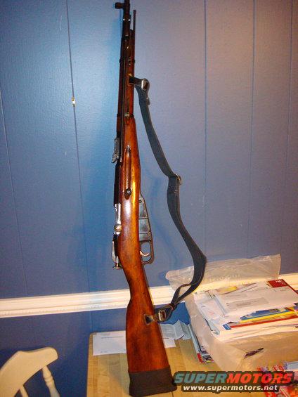 Wooden rifle with black sling against blue wall