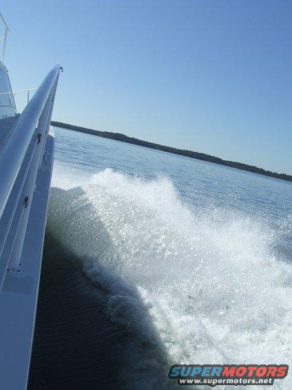 View from a moving boat showing a large wake and the side of the boat