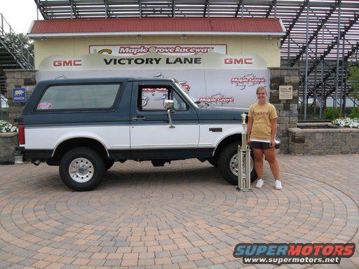 1995 Ford Bronco side view, blue and white, with woman and trophy at Victory Lane