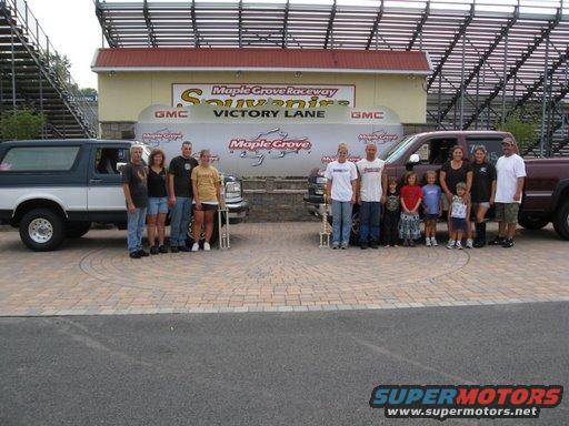 Two-tone SUV and a pickup truck with families in front of a victory lane sign at Maple Grove Raceway