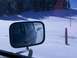 1979 Ford Bronco - A convoy of vehicles travels down a snow-covered road, seen through the side mirror of a green vehicle.