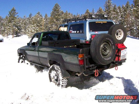 Green pickup truck and blue SUV parked in snow, both with off-road tires and modifications