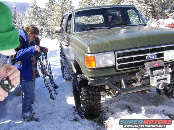 Green Ford Bronco with winch in snow, people preparing chains