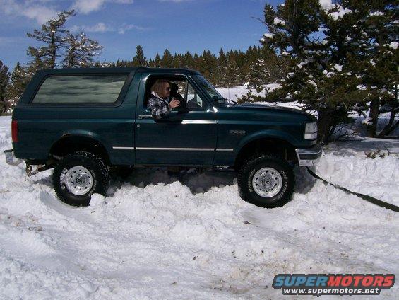 Green Ford Bronco stuck in deep snow, driver visible inside