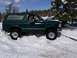 1979 Ford Bronco - A green Ford Bronco is stuck in a snowdrift, with trees and a blue sky in the background.