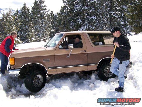 Ford Bronco stuck in deep snow, two people trying to free it
