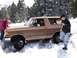 1979 Ford Bronco - A person pushes the front of a stuck Ford Bronco while another digs snow away from the tires.