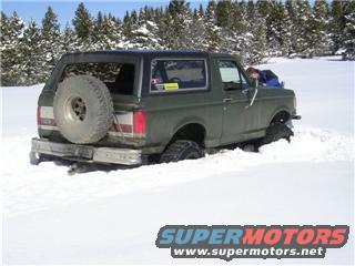 Green 1978 Ford Bronco stuck in deep snow, spare tire mounted on rear door