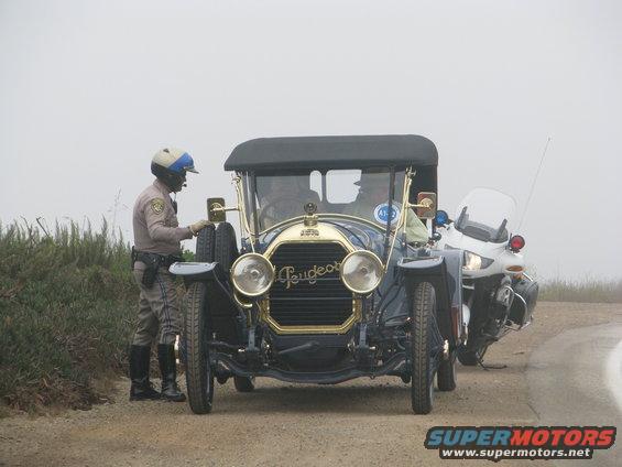 Cop talking to driver of old Peugeot car next to a police motorcycle