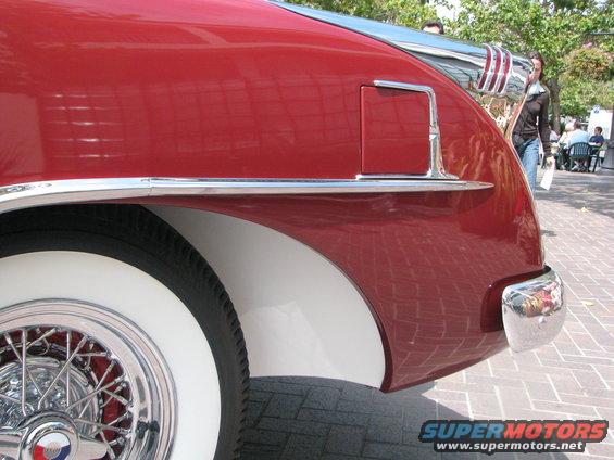 Red classic car rear quarter panel with chrome trim and whitewall tire