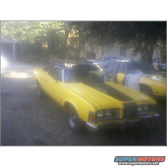 Yellow 1973 Mercury Cougar with black racing stripes, parked outdoors