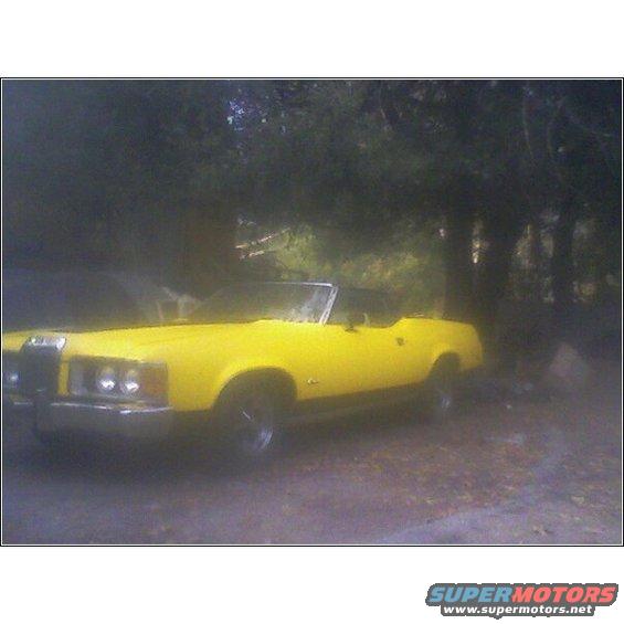 Yellow 1973 Mercury Cougar convertible parked on dirt road with trees in background