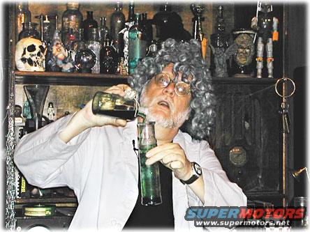 Man in a lab coat and wig pours liquid from one bottle to another in a room filled with shelves of bottles and oddities