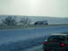 1995 Mercury Grand Marquis - A semi-trailer truck has tipped into a snow-covered ditch on a winter day, as seen from the perspective of a car.