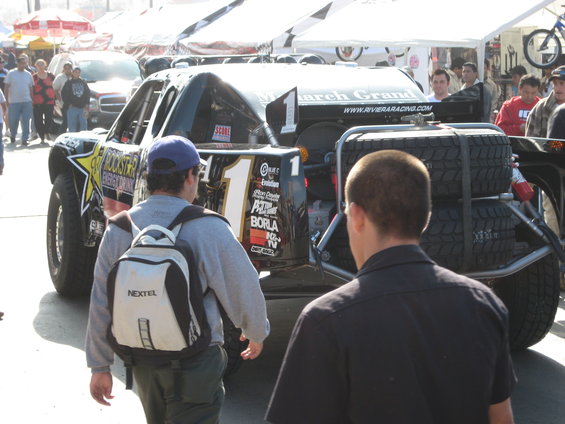Black off-road race truck with spare tires mounted on the rear, number 1 on the tailgate, and sponsor decals
