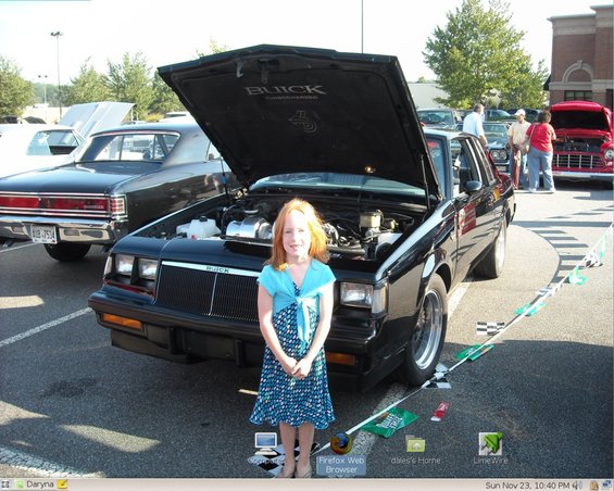 Girl in blue dress stands before black Buick Grand National, hood open. Other cars visible in background