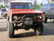 1972 Ford Bronco - Orange Ford Bronco with a winch and custom bumper is parked next to another Bronco.