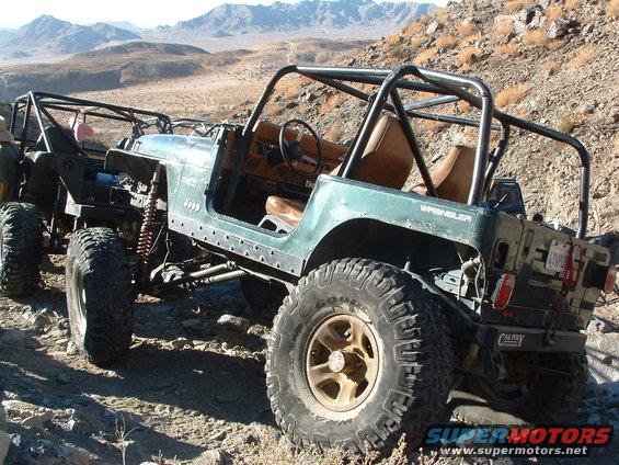 Two modified green Jeeps on a rocky desert trail. The front Jeep has a roll cage and exposed interior. The rear Jeep is partially visible
