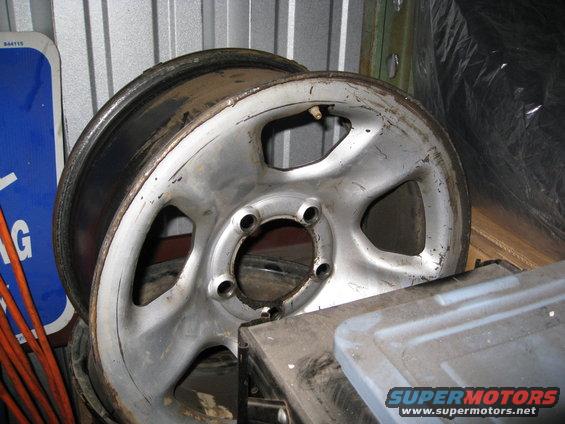 worn aluminum wheel rim with five lug holes, sitting on a metal box