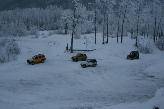 Four SUVs driving on a snow-covered road with trees in the background