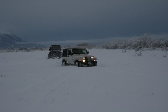 White Jeep Wrangler driving in snow, with another Jeep behind it