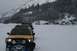 1990 Chevrolet Suburban - A yellow Nissan Xterra leads a convoy of vehicles through a snowy landscape with snow-covered mountains in the background.