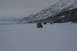 1990 Chevrolet Suburban - Multiple vehicles traverse a vast snowy landscape under a cloudy sky, with a snow-capped mountain range visible.