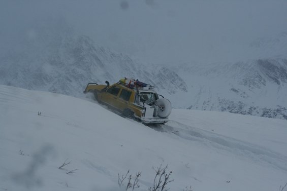 Yellow SUV with roof rack and spare tire on rear, driving on a snowy mountain slope
