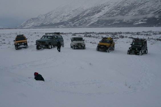 Several off-road vehicles parked in deep snow with mountains in the background