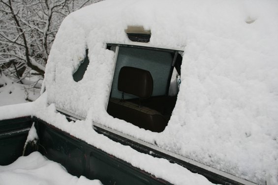 Dark green truck bed covered in snow, with a snow-covered cab interior visible through a partially cleared window