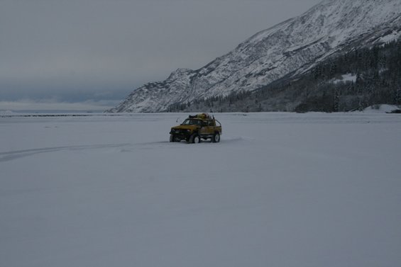 Yellow pickup truck driving on a snowy plain with mountains in the background