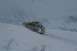 1990 Chevrolet Suburban - A yellow SUV navigates a steep, snow-covered mountain slope, its roof rack laden with gear and a spare tire mounted at the rear.