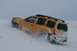 1990 Chevrolet Suburban - A yellow SUV navigates a snow-covered landscape, its tires churning through the deep snow.