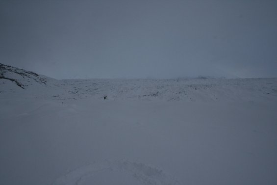 Snowy landscape with a person standing in the distance near a glacier