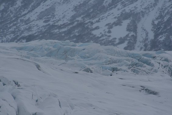 Snow-covered glacier with blue ice formations under a cloudy sky