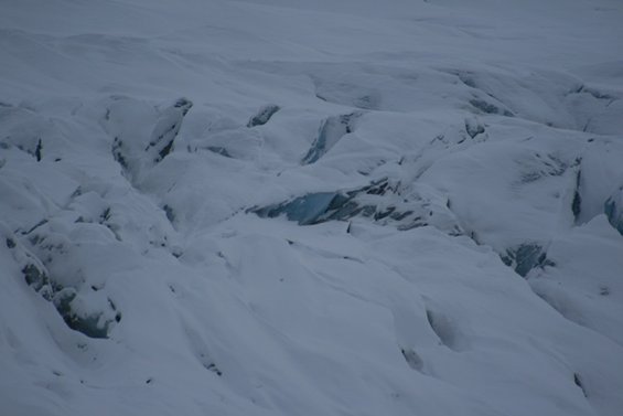 Snowy glacier surface with deep crevasses and blue ice visible in some cracks