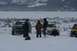 1990 Chevrolet Suburban - Several vehicles are stuck in the snow near a frozen lake with a wooded mountain range in the background.
