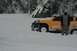 1990 Chevrolet Suburban - An orange SUV is stuck in deep snow, with a person standing next to it in a snowy landscape.