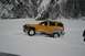 1990 Chevrolet Suburban - A yellow SUV navigates a snowy landscape, its front bull bar visible as it drives through deep snow.