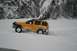 1990 Chevrolet Suburban - A yellow SUV navigates a snowy landscape with a mountainous, tree-lined backdrop.